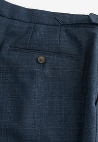 Navy blue tailored pants with a textured fabric, featuring a single back pocket and a brown button detail.