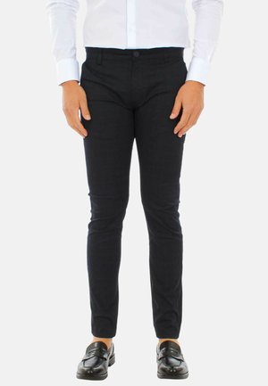 Pantaloni neri su misura con una vestibilità slim, texture liscia e un motivo sottile, abbinati a una camicia bianca e mocassini neri.