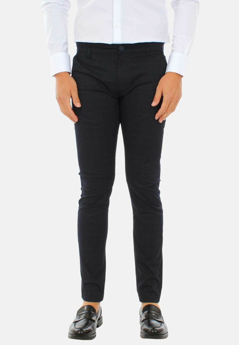 Pantaloni neri su misura con una vestibilità slim, texture liscia e un motivo sottile, abbinati a una camicia bianca e mocassini neri.