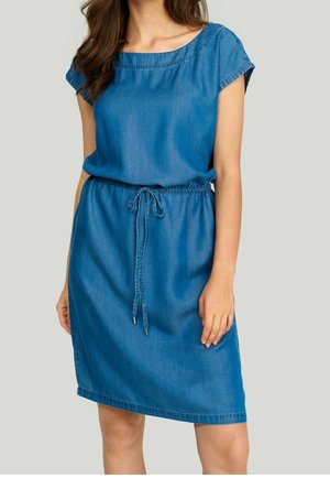 Woman wearing knee-length blue denim dress with cap sleeves and adjustable drawstring waist, standing against neutral background.