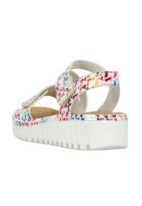 Sandales blanches avec un design multicolore et tacheté. Elles présentent une sangle ajustable et une semelle texturée et épaisse. Vue de côté.