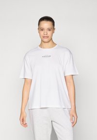 Tricou alb din bumbac, cu mâneci scurte, decolteu rotund și un logo imprimat centrat "ATHLEISURE". Asortat cu pantaloni de trening gri deschis.