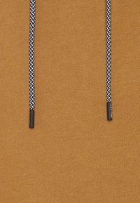 Tissu en maille brun avec une surface texturée, doté d'un cordon de serrage noir et blanc à motif, avec une extrémité en plastique et un détail de marque.