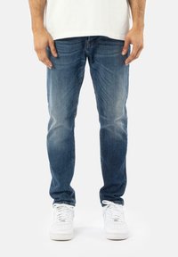 Vaqueros de mezclilla azul de corte slim, con un lavado desgastado, diseño clásico de cinco bolsillos y terminados con zapatillas blancas.