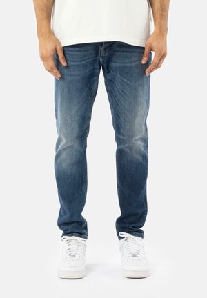 Blå denim jeans med slim fit, med en falmet vask, klassisk fem-lomme-design og afsluttet med hvide sneakers.