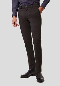 Zwarte katoenen chinos met een slim fit, voorzien van voorzakken, een knoopsluiting en een gladde textuur. Gepaarde met zwarte leren laarzen.