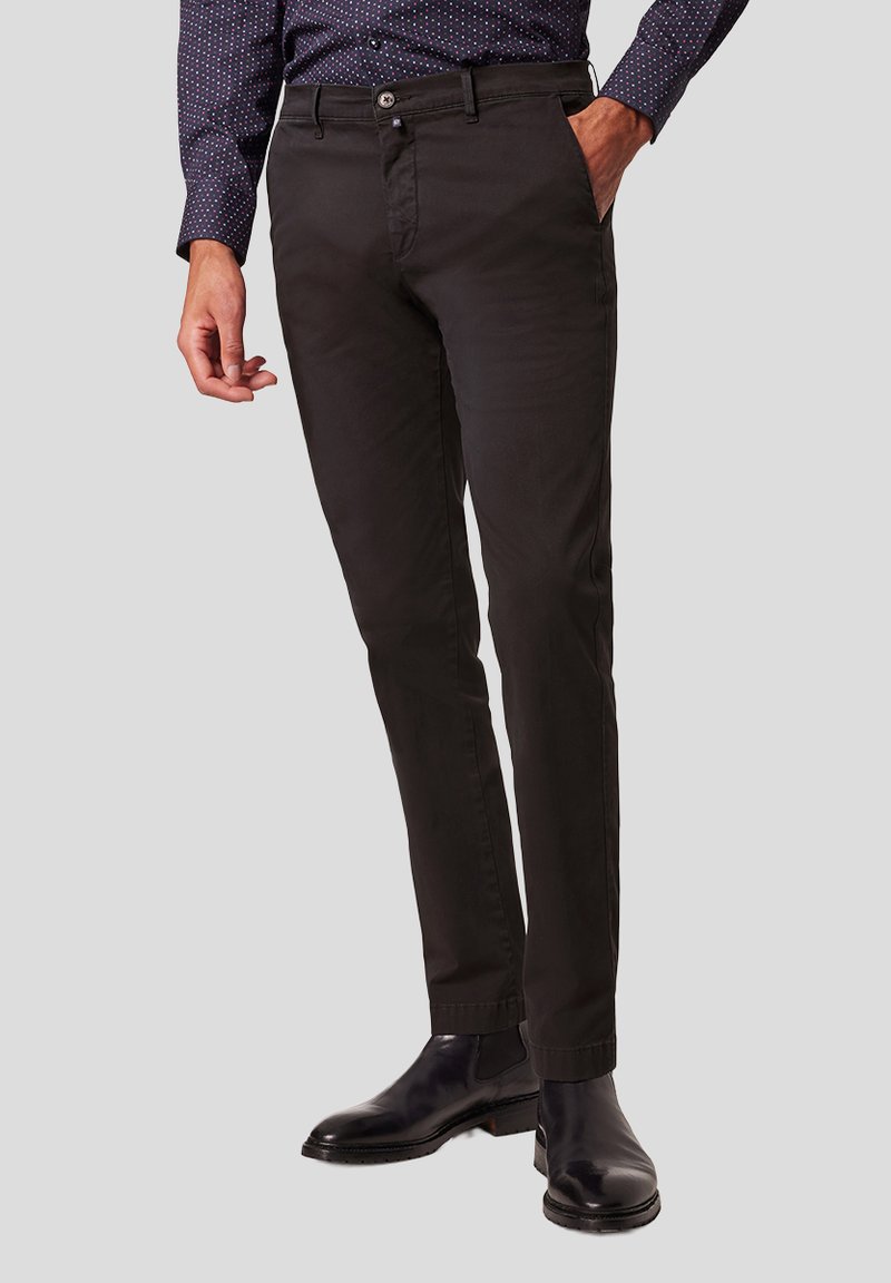 Zwarte katoenen chinos met een slim fit, voorzien van voorzakken, een knoopsluiting en een gladde textuur. Gepaarde met zwarte leren laarzen.