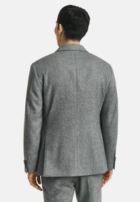 Grau gestreifter Anzugjacke mit tailliertem Schnitt, Reverskragen und zwei Knöpfen, von hinten betrachtet. Merkmale sind detaillierte Nähte und ein strukturiertes Gewebe.