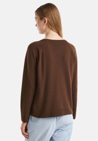 Maglione marrone a maglia con una vestibilità rilassata, maniche lunghe e colletto girocollo. La texture sembra morbida, adatta per un abbigliamento casual.