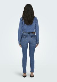 Denim jakna in prilegajoče jeans, oboje v srednje modri barvi. Jakna ima skrajšan dizajn s strganim robom, jeans pa ima zadnja žepek.