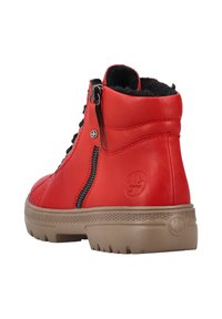 Bottine en cuir rouge avec une finition texturée, fermeture éclair sur le côté, lacets noirs et semelle en caoutchouc beige avec un motif de semelle. Logo embossé sur le talon.