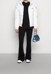 Hvid dunjakke med aftagelig hætte, sort t-shirt og sorte udvidede bukser. Lille blå tie-dye håndtaske og hvide sneakers.