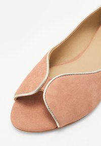 Helle rosa Wildlederflatschuhe mit offenem Zeh, die ein geschwungenes Design und einen kontrastierenden crèmefarbigen Rand entlang der Kanten aufweisen. Glattes Innenfutter.
