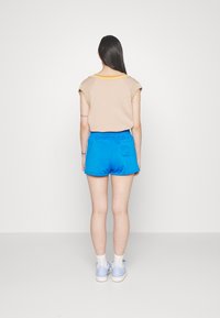 Beige kortärmad topp med orange och gula accenter, kombinerad med blå shorts med resår i midjan och en bakficka.