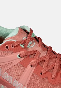 Scarpa sportiva rossa e menta con tomaia in rete, sovrapposizioni testurizzate e lacci piatti. Presenta il logo sul lato e un design della suola a contrasto.