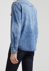 Jeansskjorta i ljusblått, med knäppte manschetter och spetsig krage, med en strukturerad yta och kontrasterande sömdetaljer.