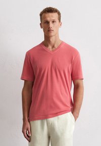 T-shirt corail en V fabriqué en coton doux, avec des manches courtes et une coupe décontractée, associé à un pantalon en lin de couleur claire.