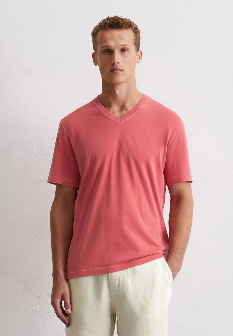 T-shirt corail en V fabriqué en coton doux, avec des manches courtes et une coupe décontractée, associé à un pantalon en lin de couleur claire.