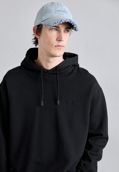 Black hoodie with an embroidered "NN. 07" logo. Complemented by a light blue, distressed denim cap with a frayed brim.