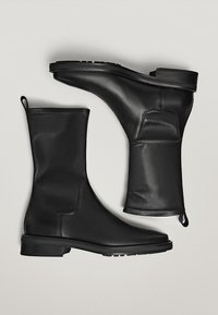 Bottines en cuir noir avec une texture lisse, présentant un talon bloc bas et une languette, conçues avec une silhouette élégante et un minimum de détails.