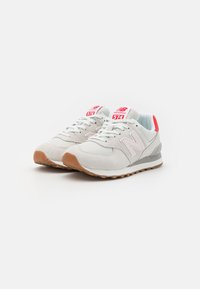 Light gray New Balance 574 sneakers with mesh and suede upper, pink accents, white laces, and a gum rubber outsole.