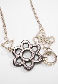 Collier en chaîne argentée avec pendentif fleur noire aux détails ajourés, un charme triangulaire et des éléments circulaires entrelacés.