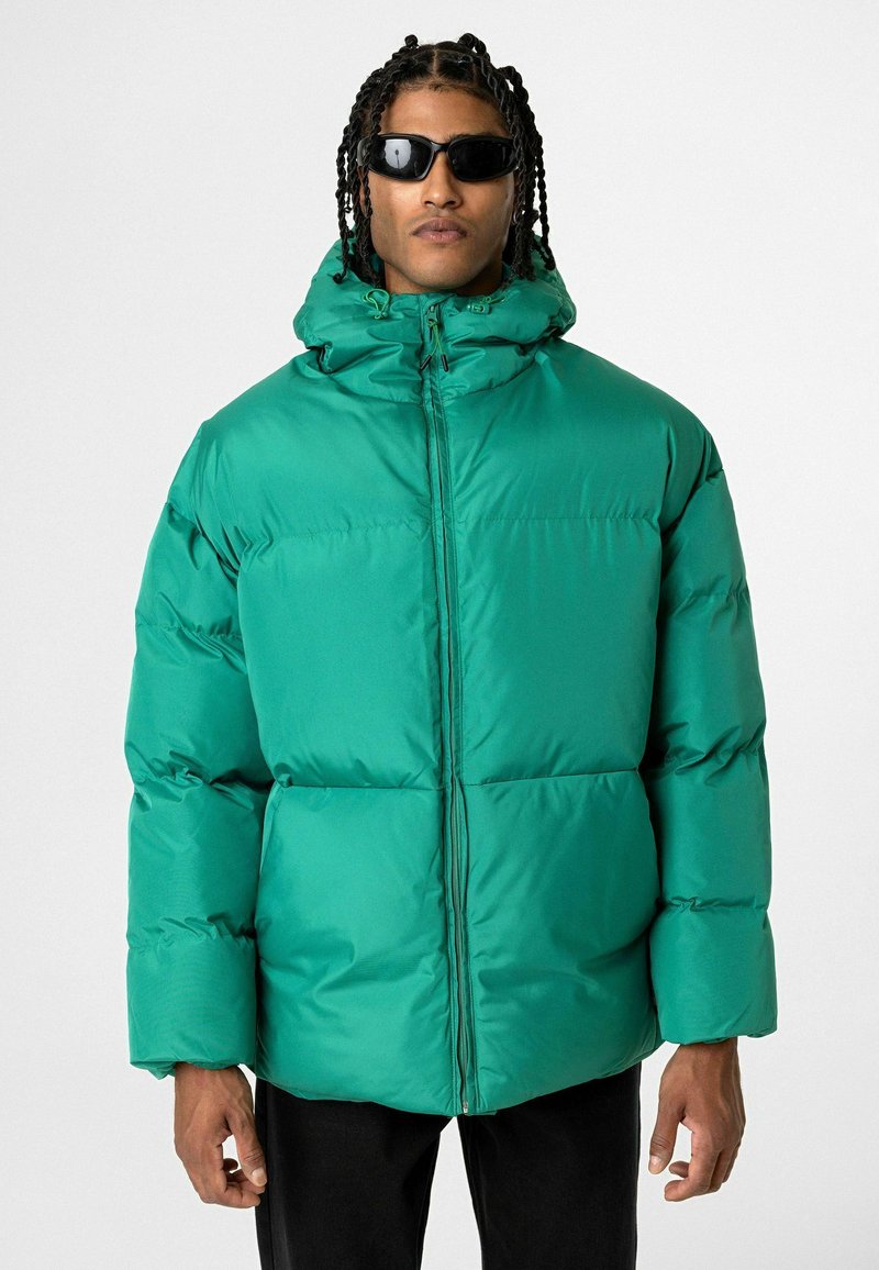 Groene pufferjack met een hoge kraag, rits sluiting en brede mouwen. Glad, glanzend materiaal met een boxy vorm en gewatteerd ontwerp.