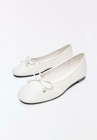 Fehér bőr balettcipő kerek orral, apró masnikkal az elején és fekete lapos talppal.