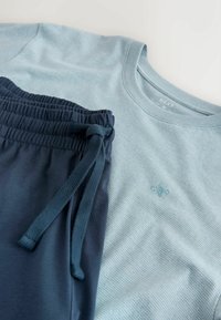 Chemise à manches courtes à rayures bleu clair avec petit logo, associée à un pantalon bleu marine à taille élastique avec cordon de serrage, étalée à plat sur une surface blanche.