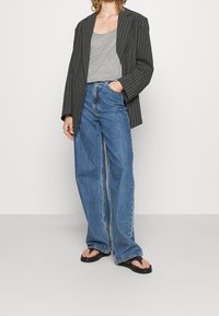Gestreepte zwarte blazer, grijze tanktop en losse blauwe jeans. Draag met zwarte flip-flops. Belangrijkste kenmerken zijn de relaxte pasvorm en casual stijl.