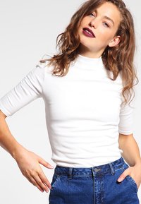Hvit ribbet turtleneck genser med korte ermer, kombinert med høyt liv blå denimjeans med knapplukking og sidelommer.