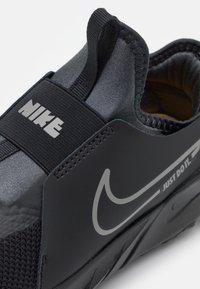 Czarny but sportowy z teksturowaną cholewką, elastycznym paskiem i wyraźnym logo Nike. Projekt obejmuje gładki, opływowy kształt.