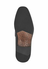 Schwarze Gummisohle mit strukturierter Oberfläche, versehen mit einem braunen Lederakzent in ovaler, gemusterter Form und geprägtem "Tamaris"-Logo.