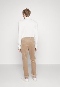 Pantalones de pana beige con un diseño de pierna recta, combinados con una camisa ajustada de manga larga blanca y zapatillas blancas. Puños enrollados visibles.