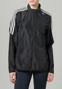 Black lightweight jacket with zip front, high collar, and three white stripes on each shoulder. Made of smooth, shiny fabric.