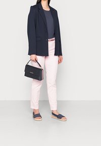 Námořnický blazer, šedý top, světle růžové kalhoty, námořnické sandály a černá kabelka se zlatým logem. Vyznačuje se štíhlým střihom a elegantním designem.