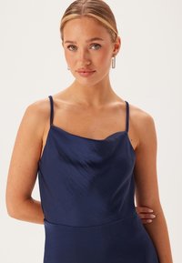 Marinblå satin camisole med tunna spagettiremmar, mjuk draperad halsringning och slät struktur som framhäver en figursydd design.