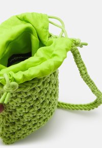 Borsa verde intrecciata con cordino e tracolla intrecciata, parzialmente aperta che mostra l'etichetta interna.