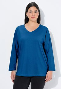 Koszula z długim rękawem i dekoltem w serek w jednolitym niebieskim kolorze, wykonana z miękkiej tkaniny o luźnym kroju, z prostym dołem i minimalnymi zdobieniami.