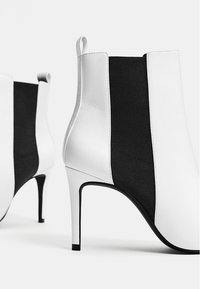 Botines en blanco y negro hechos de cuero y tela, con un alto tacón de aguja y una lengüeta en la parte trasera.