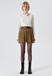Top bianco a maniche lunghe con dettaglio annodato, gonna plissettata color khaki, collant neri trasparenti e stivaletti neri con lacci e suola spessa.