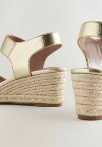 Sandali a zeppa metallici oro con tacco in juta intrecciata, apertura sul retro e larghe fasce con superficie texture.