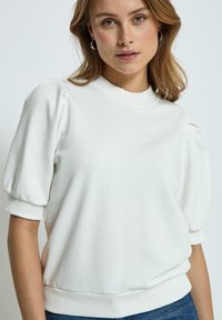 Vit sweatshirt med korta, puffiga ärmar och ribbat halsringning och muddar. Mjuk textur, avslappnad passform, kombinerad med denim.