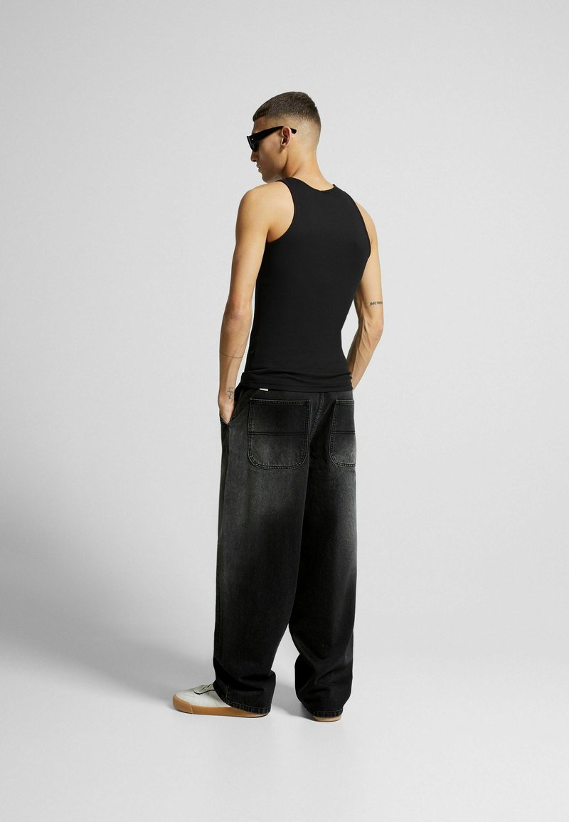 Canotta nera con design aderente, abbinata a jeans grigi scuri con vestibilità ampia e tasche posteriori. Sneakers bianche completano il look.