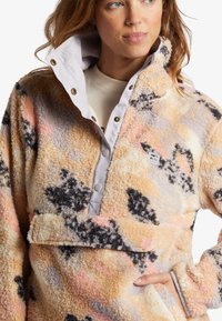 Fleece-pullover i pastelfarver med sorte og grå mønstre. Har en trykknapkrave og frontlomme, blød tekstur.