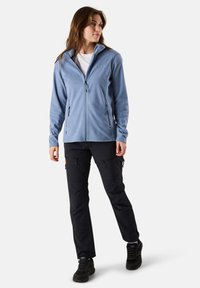 Giacca in pile azzurro chiaro con collo alto, zip frontale e due tasche laterali. Abbinata a pantaloni cargo neri con tasche con zip.