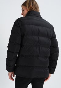 Sort pufferjakke med høj krave og quiltet design. Har en glat, shiny tekstur og markante vandrette syninger.
