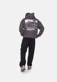 Felpa grigia con stampa grafica che rappresenta la Torre Eiffel, abbinata a pantaloni neri e sneaker di colore chiaro. Design casual, vestibilità rilassata.