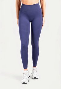 Leggings bleu marine taille haute en tissu extensible, dotés d'une ceinture côtelée et d'une texture lisse. Accompagnés de chaussures de sport blanches.