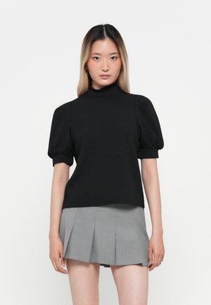 Svart topp med pufferm, høy hals, laget av teksturert materiale. Kombinert med et grått plisserte skjørt, med et enkelt, strømlinjeformet design.